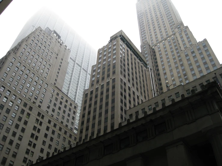 some very tall buildings in a big city, inspired by Hugh Ferriss, flickr, under a gray foggy sky, wall street, photo taken from the ground, buildings carved out of stone