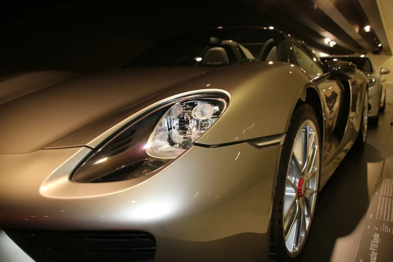 a silver sports car is on display in a showroom, a picture, inspired by Harry Haenigsen, pexels, photorealism, front light, liquid gold, upward shot, porche