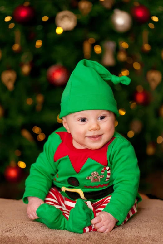 a baby sitting in front of a christmas tree, inspired by Ernest William Christmas, happening, portrait of very beautiful elf, portrait mode photo, green clothes, very very happy!