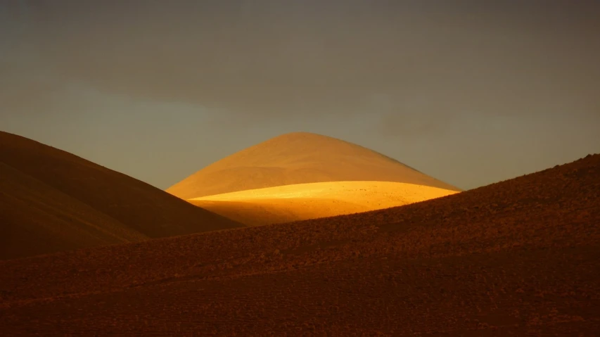 a large mountain in the middle of a desert, a picture, by Andrei Kolkoutine, flickr, land art, back lit lighting, salt dunes, mayo, gold dappled light