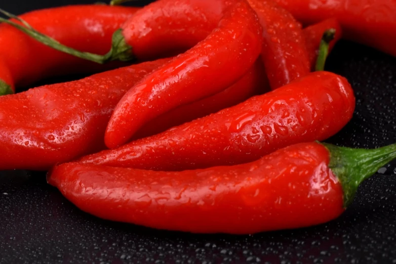 a pile of red hot peppers sitting on top of a black surface, a digital rendering, pixabay, fantastic realism, closeup 4k, wet from rain, solid background, red round nose