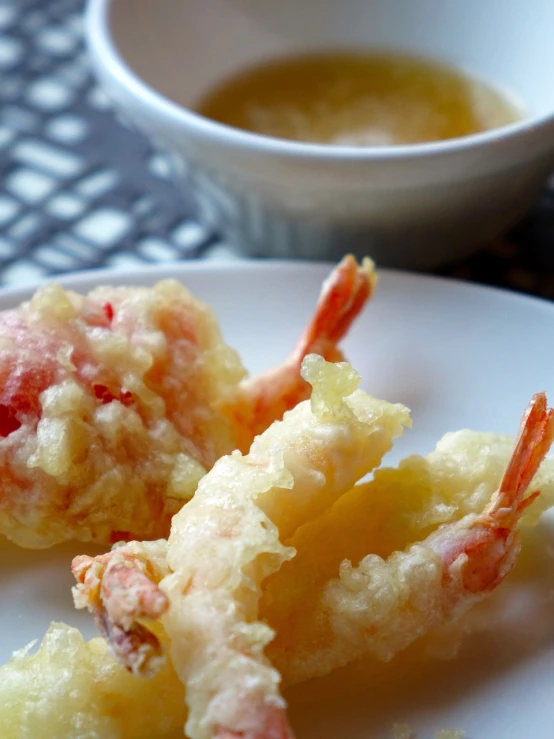 a white plate topped with fried shrimp next to a bowl of soup, sōsaku hanga, closeup photo, battered, resin, fruit