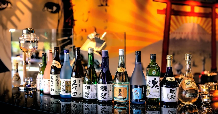 a group of wine bottles sitting on top of a bar, a picture, inspired by Kanō Shōsenin, edited, with a drink, asia, various colors