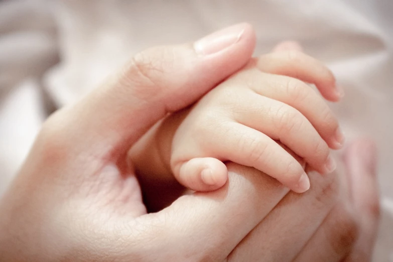 a close up of a person holding a baby's hand, shutterstock, symbolism, ad image, soft colors, enhanced photo, highly polished