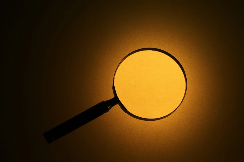 a magnifying glass sitting on top of a table, yellow lighting, circle, shade, photo - shot