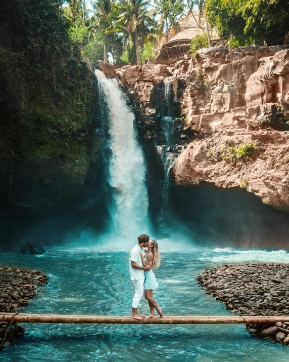 a man and a woman standing in front of a waterfall, a picture, by John La Gatta, pexels contest winner, sumatraism, love is begin of all, 💋 💄 👠 👗, flowing white robes, tropical paradise