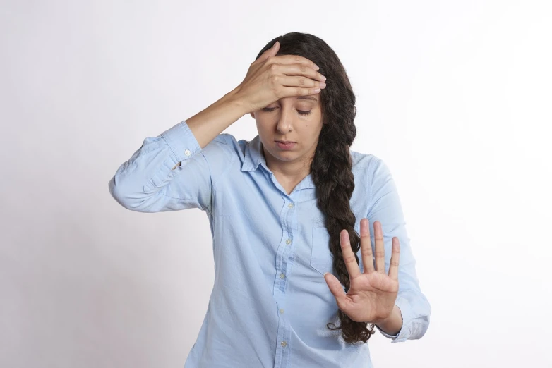 a woman holding her head in her hands, a picture, hand controlling, wearing a light blue shirt, the futility of overexertion, standing sideways