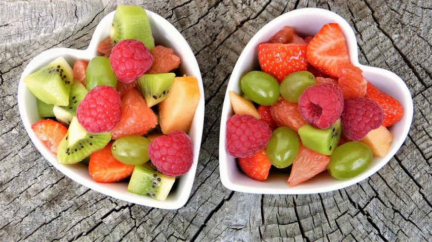 two heart shaped bowls filled with fruit on top of a wooden table, a picture, pexels, screengrab, bright and colourful, different sizes, bowl filled with food