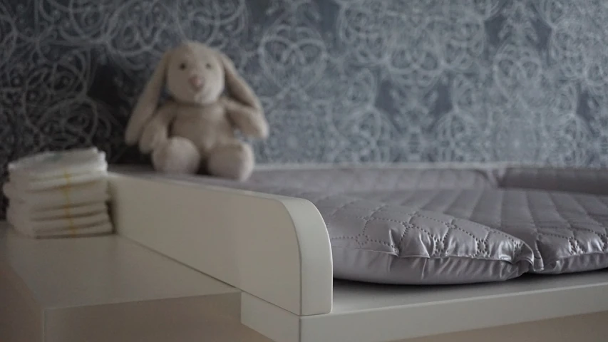 a teddy bear sitting on top of a bed next to a stack of diapers, a picture, art deco, made in tones of white and grey, wallpaper!, closeup - view, eero aarnio