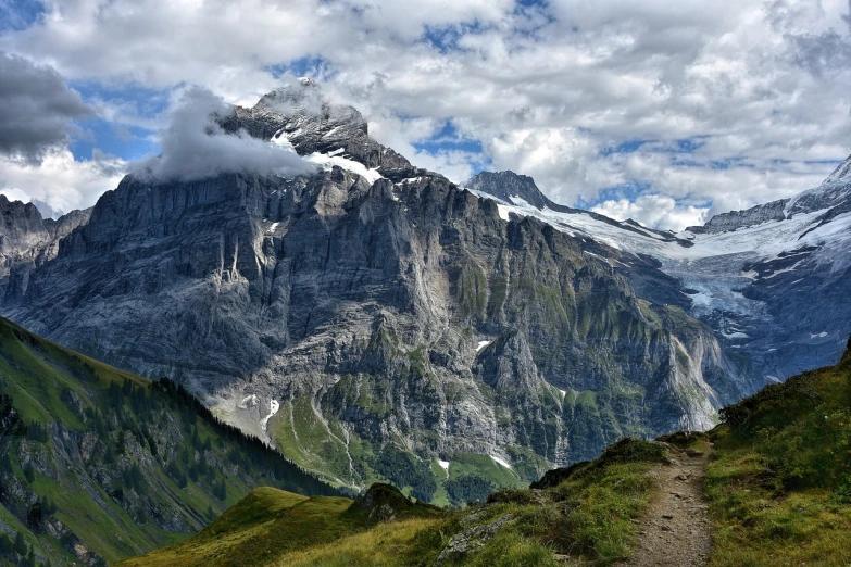 a man standing on top of a lush green hillside, a picture, by Werner Andermatt, giant imposing mountain, with a snowy mountain and ice, time to climb the mountain path, the photo shows a large