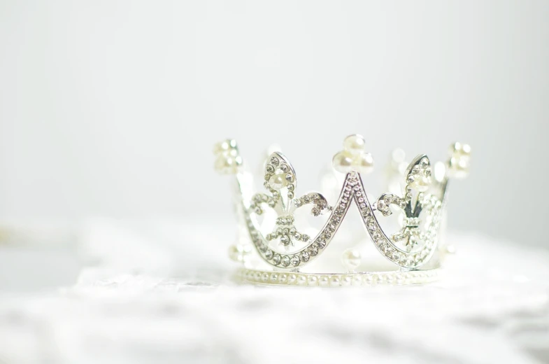 a silver crown sitting on top of a white table, a macro photograph, digital art, beautiful wallpaper, background image, ornately dressed, carnival
