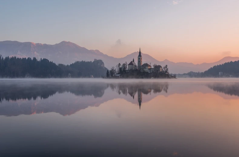 a small island in the middle of a lake, by Sebastian Spreng, light pink mist, church in the background, slovenian, paradise in the background