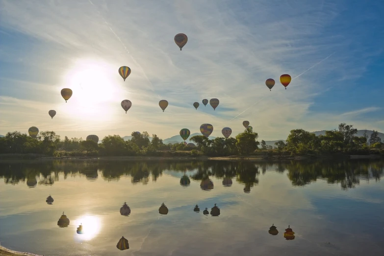 a group of hot air balloons flying over a lake, a photo, wide shot photo, beautiful rtx reflections, morning atmosphere, award winning masterpiece photo