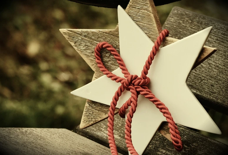 a white star sitting on top of a wooden bench, a picture, pexels, folk art, red ribbon, organic ornament, mid closeup, rope