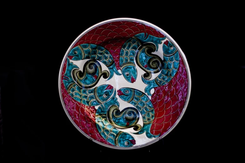 a close up of a plate with a design on it, inspired by Paul Howard Manship, cloisonnism, swirling silver fish, magenta and crimson and cyan, commercial product photography, intertwined full body view