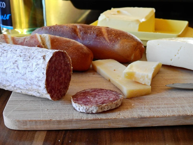 a wooden cutting board topped with different types of cheese, dau-al-set, sausage, baking french baguette, close to the camera, recipe