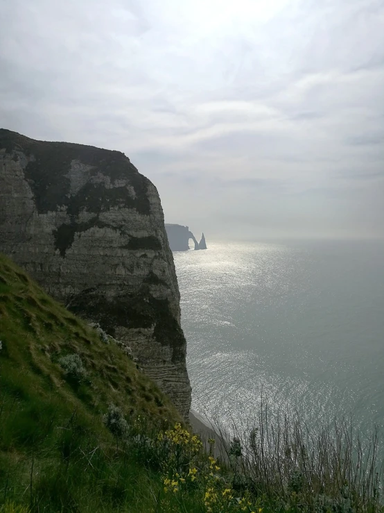 a man standing on top of a cliff next to the ocean, a picture, by Edward Corbett, les nabis, northern france, big sharp rock, viewed from very far away, trident