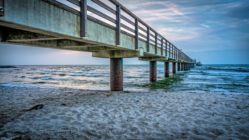 a pier sitting on top of a sandy beach next to the ocean, a portrait, by Don Reichert, pixabay contest winner, renaissance, bridge over the water, florida, concrete pillars, view from the side”