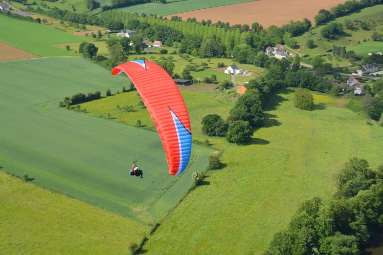 a person paragliding over a lush green field, a picture, by Juergen von Huendeberg, shutterstock, normandy, cobalt blue and pyrrol red, very high angle view, ornithopter