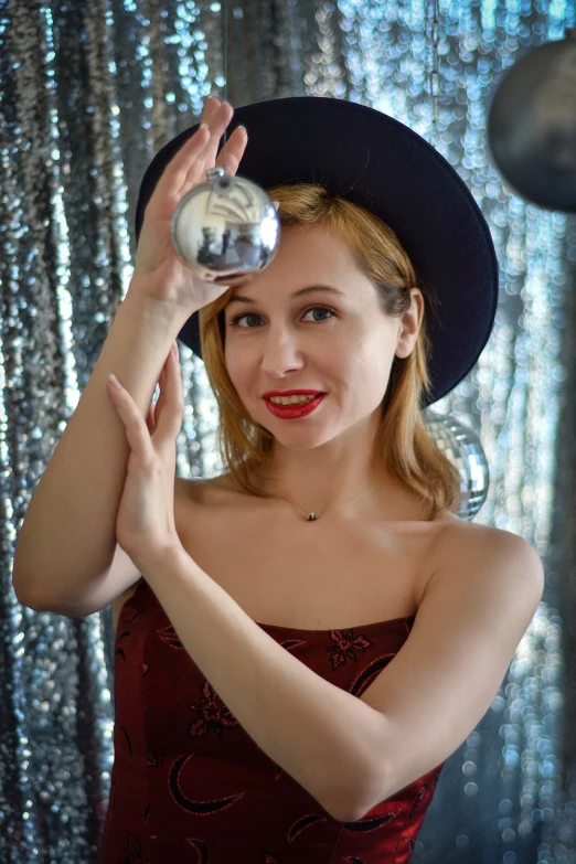 a woman in a red dress and a black hat, a portrait, tumblr, magic realism, disco ball in background, cheeky smile with red lips, in style of britt marling, glass ball