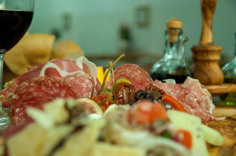 a close up of a plate of food and a glass of wine, a picture, by Jan Rustem, pexels, realism, salami, overflowing feast buffet table, 3/4 view from below, food commercial 4 k