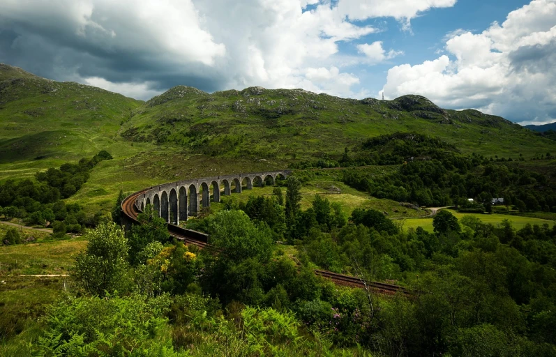 a train traveling through a lush green countryside, by Andrew Robertson, flickr, in hogwarts, rock arches, serpentine curve!!!, highlands