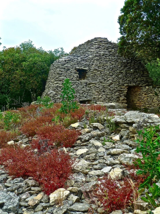 a stone building sitting on top of a lush green hillside, by Róbert Berény, les nabis, overgrown with colorful coral, traditional corsican, ancient catacombs, sculpture made of piled stones