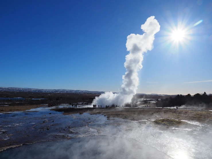 a group of people standing in front of a steaming geyse, a picture, by Hallsteinn Sigurðsson, shutterstock, hot with shining sun, blue sky, january, ground explosion