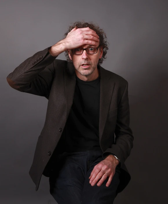 a man sitting on a chair with his hands on his head, a picture, flickr, photorealism, tim burton, 1 / 4 headshot, peter hurley, with index finger