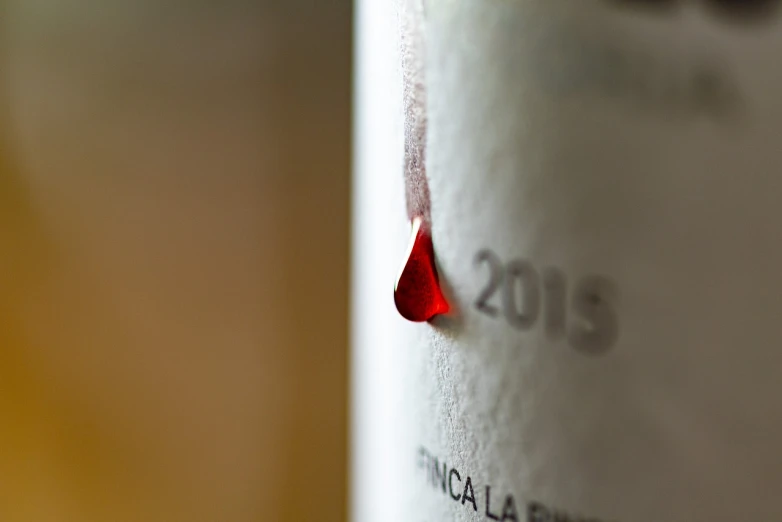 a close up of a bottle of wine on a table, by Pinchus Kremegne, flickr, process art, tear drop, silver white red details, spain, service ticket close up