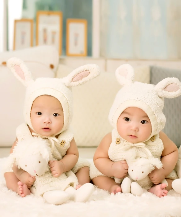 a couple of babies sitting on top of a white rug, inspired by Anne Geddes, shutterstock, bunny suit, taiwan, with a twin, gettyimages