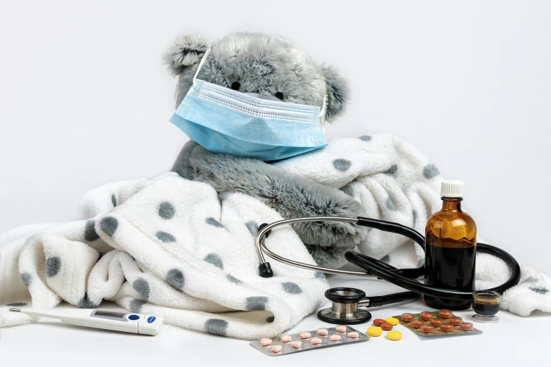 a teddy bear wrapped in a blanket next to a bottle of pills and a stethoscope, a picture, by Maksimilijan Vanka, shutterstock, plasticien, medical mask, on grey background, children's, group photo