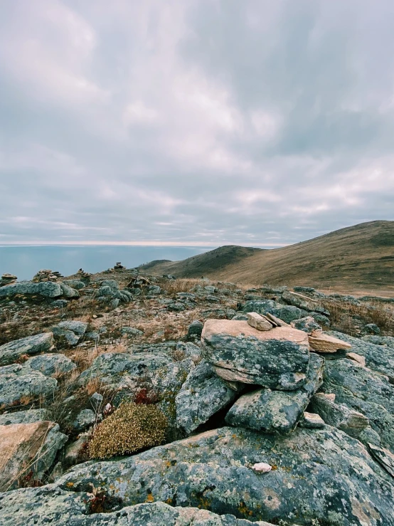 a pile of rocks sitting on top of a mountain, a picture, by Alexander Runciman, visual art, near lake baikal, overcast! cinematic focus, tundra, ultrawide angle cinematic view