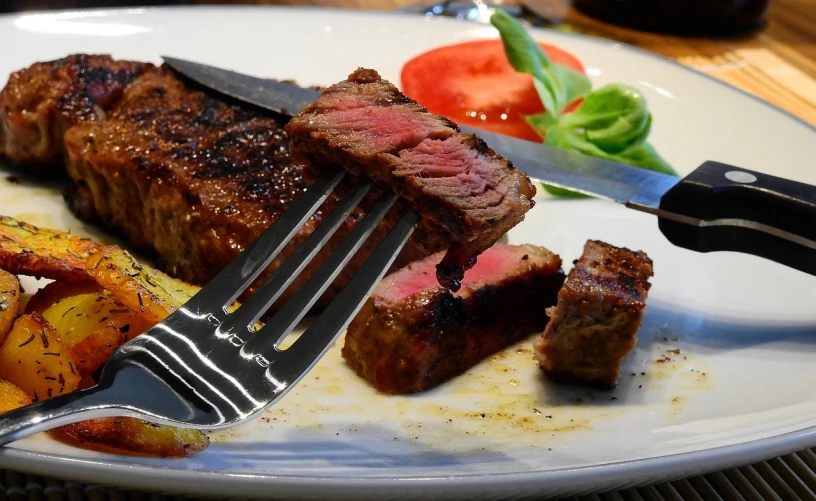 a close up of a plate of food with a knife and fork, a picture, by Tom Wänerstrand, pixabay, realism, steak, carnivorous, yoshiku, right side composition