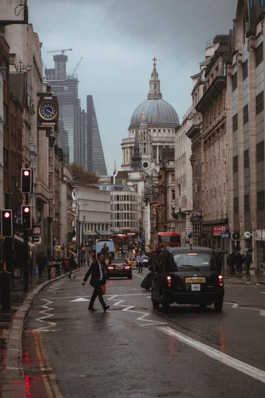 a couple of cars driving down a street next to tall buildings, inspired by Thomas Struth, pexels, nineteenth century london, people walking in street, church in the background, benjamin vnuk