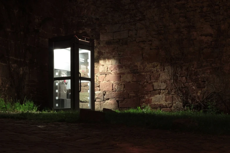 a phone booth sitting in front of a brick wall, by Jan Konůpek, volumetric outdoor lighting, located in a castle, cellar, still from l'estate