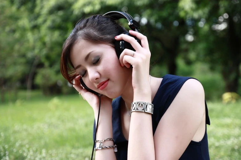 a woman holding a pair of headphones to her ear, an album cover, by Istvan Banyai, pixabay, in the park, woman is sitting, serene smile, exquisitely detailed