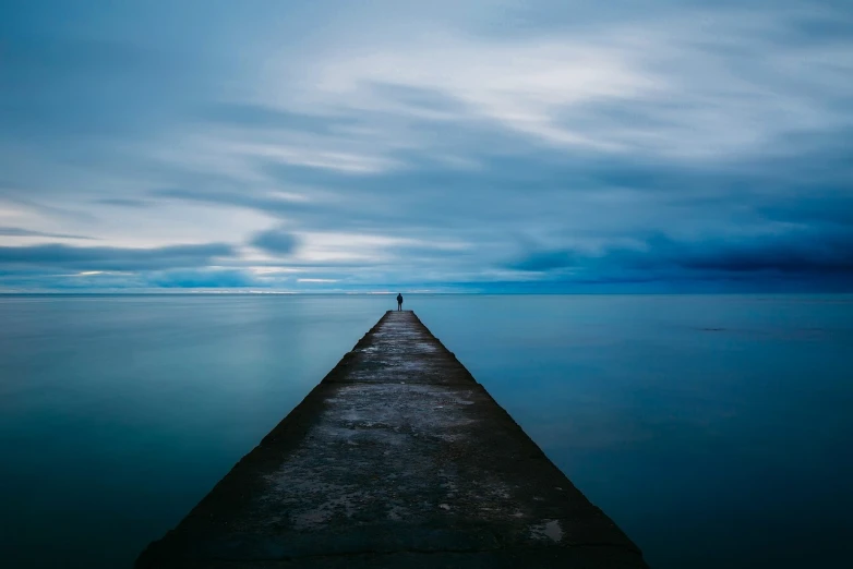 a lone person standing on the end of a pier, by Brad Holland, deep blue atmosphere, serene overcast atmosphere, trailing off into the horizon, absolutely outstanding image