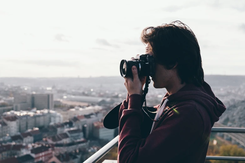 a man taking a picture of a city with a camera, by Matthias Weischer, unsplash contest winner, petzval lens. featured on flickr, looking up at camera, profile shot, stock footage