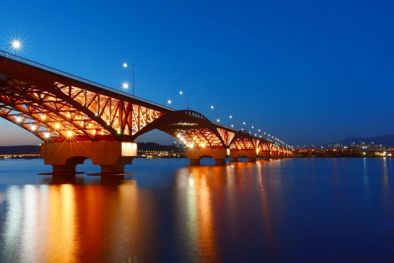 a bridge over a body of water at night, by Bernardino Mei, shutterstock, pyongyang city, red trusses, summer evening, hi-res photo