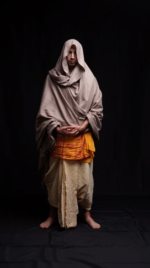 a man standing in front of a black background, inspired by Georges de La Tour, hurufiyya, somali woman, full body picture of a male monk, covered with blanket, medieval dress yellow ochre