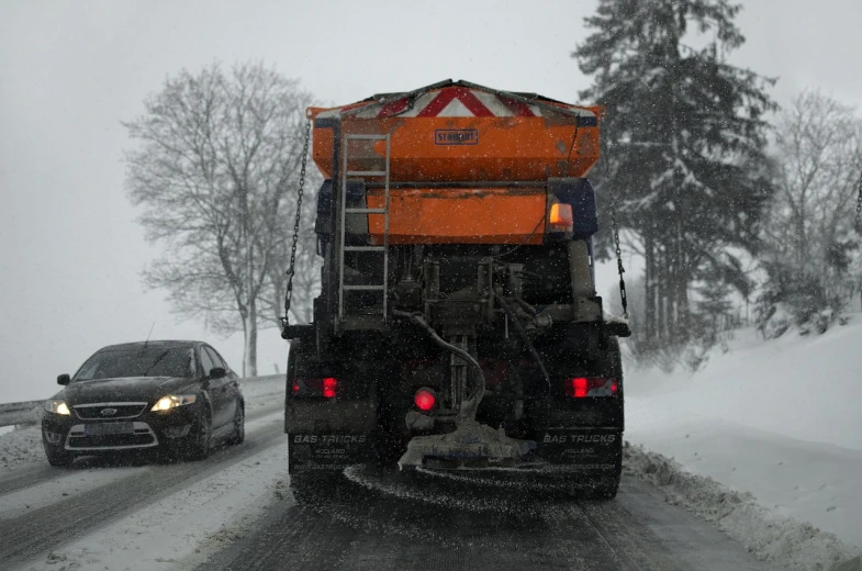 a truck driving down a snowy road next to a car, plasticien, grey orange, afp, digging, rear facing