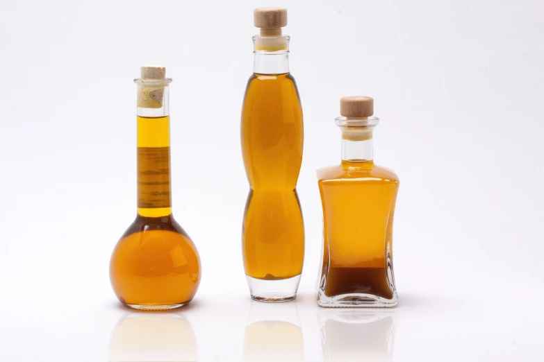 three bottles of olive oil sitting next to each other, a picture, minimalism, scientific glassware, caramel, 3 4 5 3 1, vessels