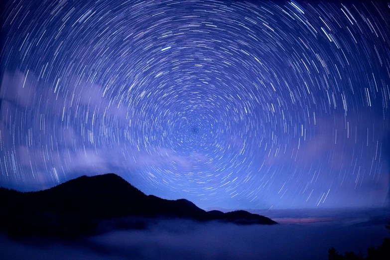 a mountain with a star trail in the sky, by Tadashige Ono, istockphoto, cloud vortex, clematis like stars in the sky, extremely high definition shot