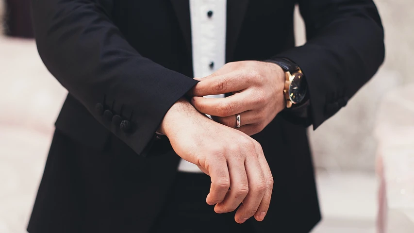 a man in a tuxedo adjusts his watch, a stock photo, shutterstock, holding hands, wearing two metallic rings, cinematic outfit photo, background image