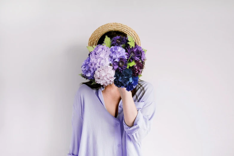 a woman covering her face with flowers in front of her face, a picture, purple outfit, with straw hat, soft blue tones, with a white background