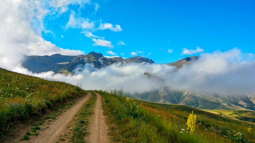 a dirt road going up a hill with mountains in the background, by Werner Andermatt, shutterstock, romanticism, covered in clouds, russia, iphone photo, atlach - nacha