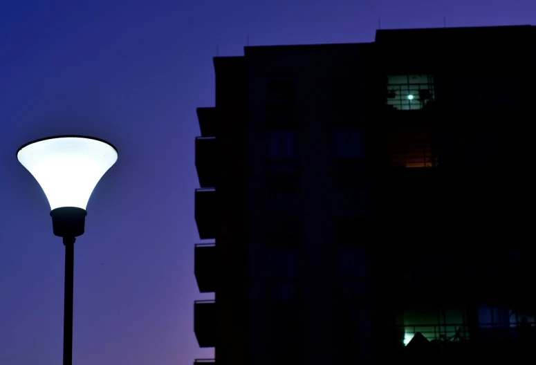 a street light in front of a tall building, a photo, by Andrei Kolkoutine, unsplash, apartment building on the moon, blue and purle lighting, banner, shot with canon 5 d mark ii