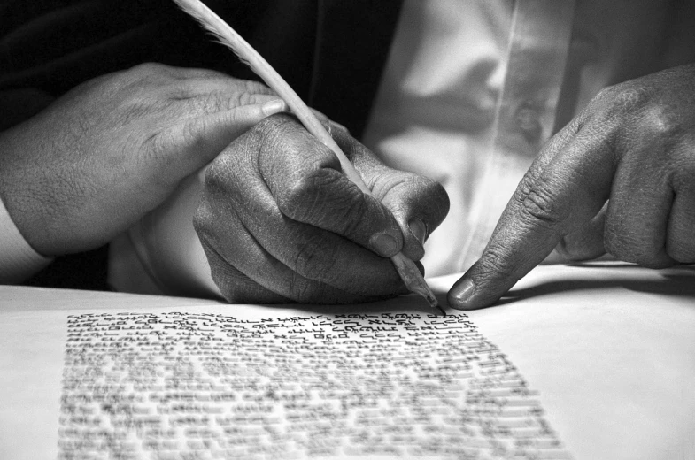 a close up of a person writing on a piece of paper, by Ken Elias, biblical image, black and white color photograph, hebrew, post-processed