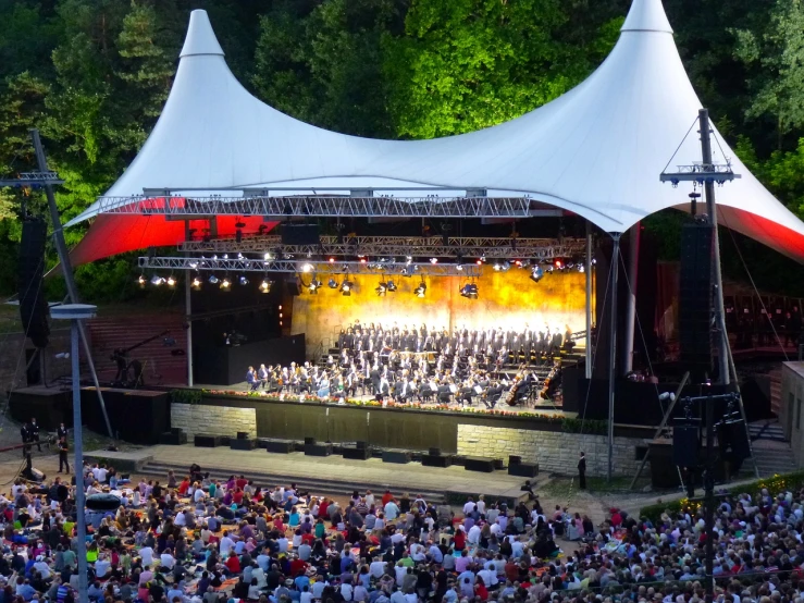 a large group of people standing on top of a stage, by Caroline Mytinger, shutterstock, black forest, orchestra, covered outdoor stage, detailed image